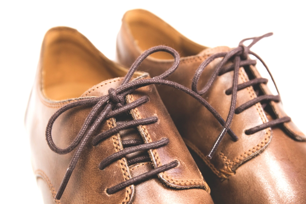 Brown leather shoes with dark laces on a plain background